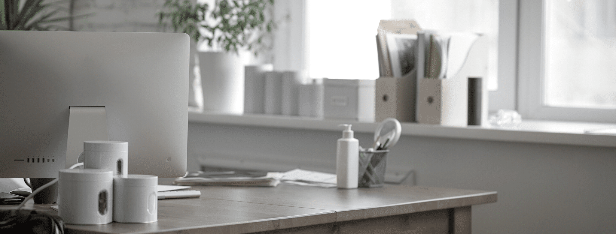 Bureau en bois avec tasses, flacon de gel hydroalcoolique, documents, et boîtes de rangement devant une fenêtre