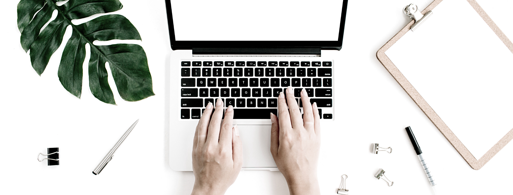 Mains tapant sur un ordinateur portable sur un bureau blanc avec plante verte, stylo, bloc-notes et accessoires de bureau